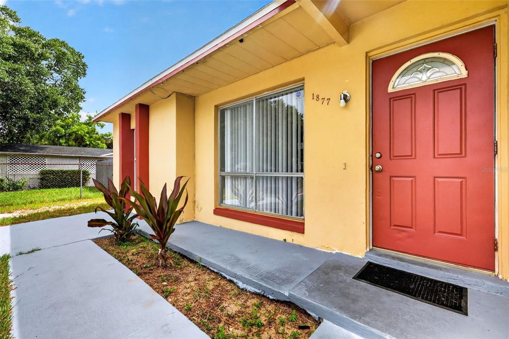 A yellow house exterior features a red front door, a large window, and a walkway — 1877 WAYSIDE DRIVE, ORLANDO, FL