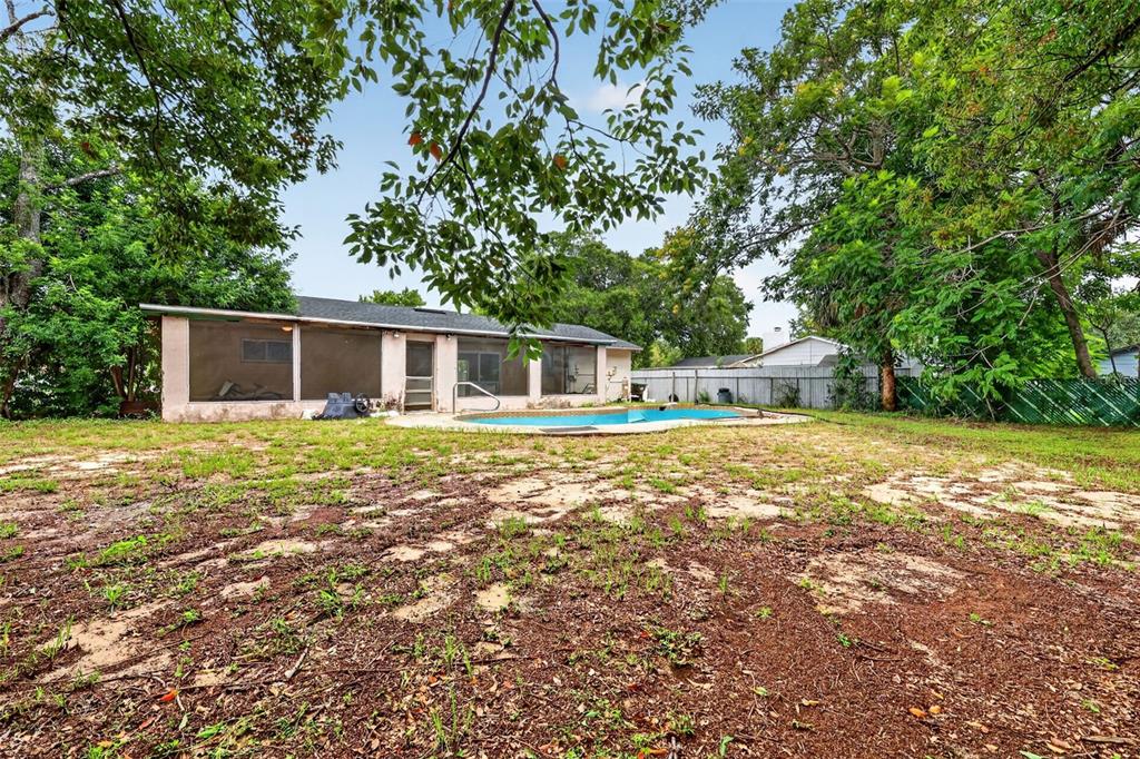 A backyard features a swimming pool, a screened-in patio, and sparse grass under large trees — 1877 WAYSIDE DRIVE, ORLANDO, FL