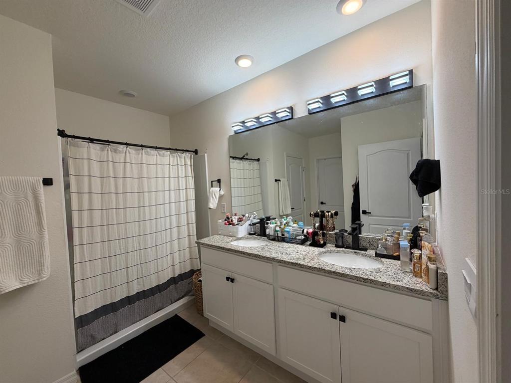 A bathroom features a double vanity with granite countertops, white cabinets, and a shower curtain — 5268 MADDIE DRIVE, HAINES CITY, FL
