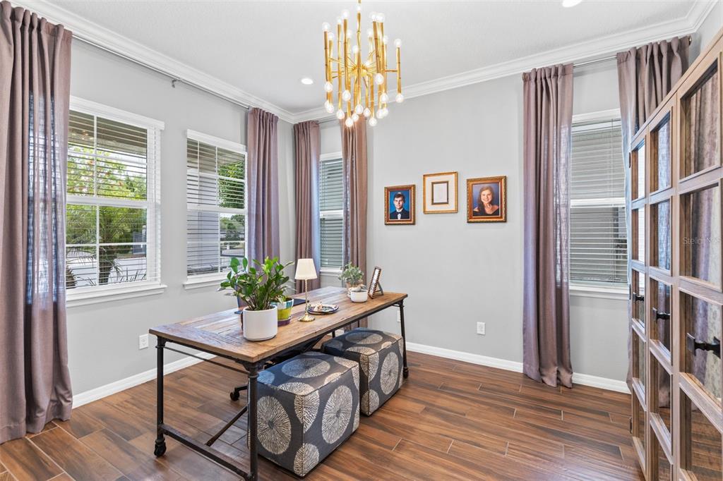 A home office features a wooden desk, patterned ottomans, a gold chandelier, and gray curtains — 1448 LAKE FLORENCE WAY, WINTER PARK, FL