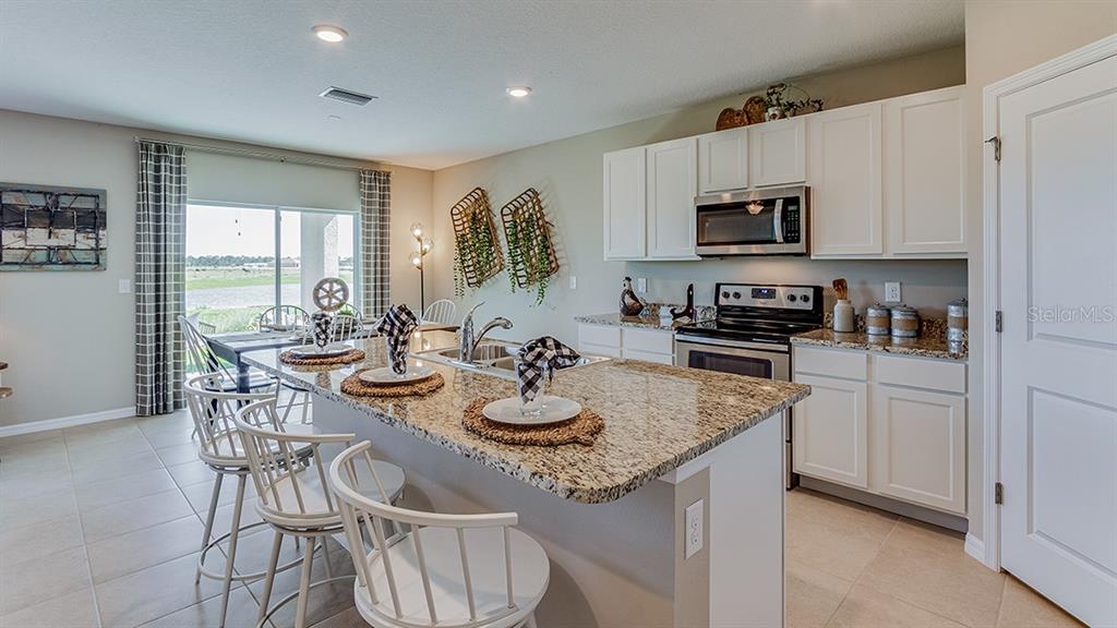 A modern kitchen features white cabinets, stainless steel appliances, a quartz island, and wood flooring — 10923 RABBIT GROVE TRAIL, PARRISH, FL