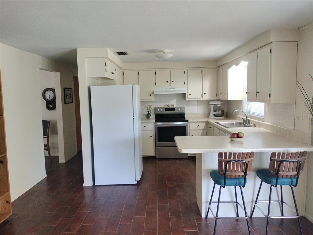 A kitchen features white cabinets, stainless steel appliances, a breakfast bar, and dark tile flooring — 39133 5TH AVENUE, ZEPHYRHILLS, FL