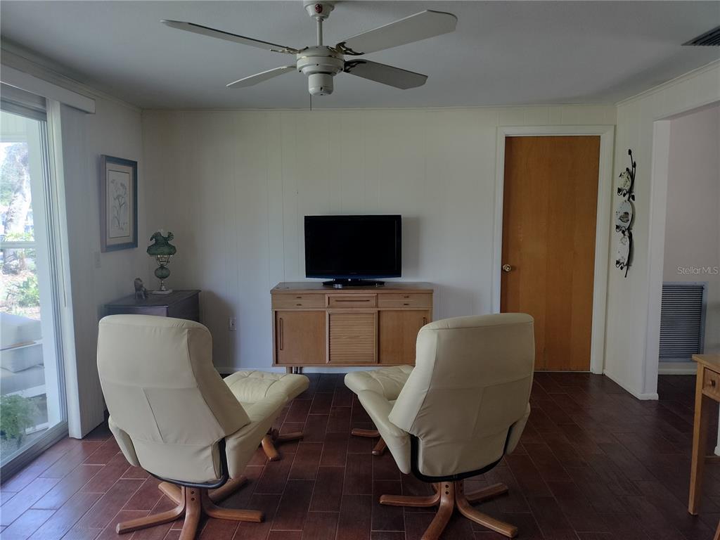 A living room features two cream-colored armchairs, a wooden media console, and dark flooring — 39133 5TH AVENUE, ZEPHYRHILLS, FL