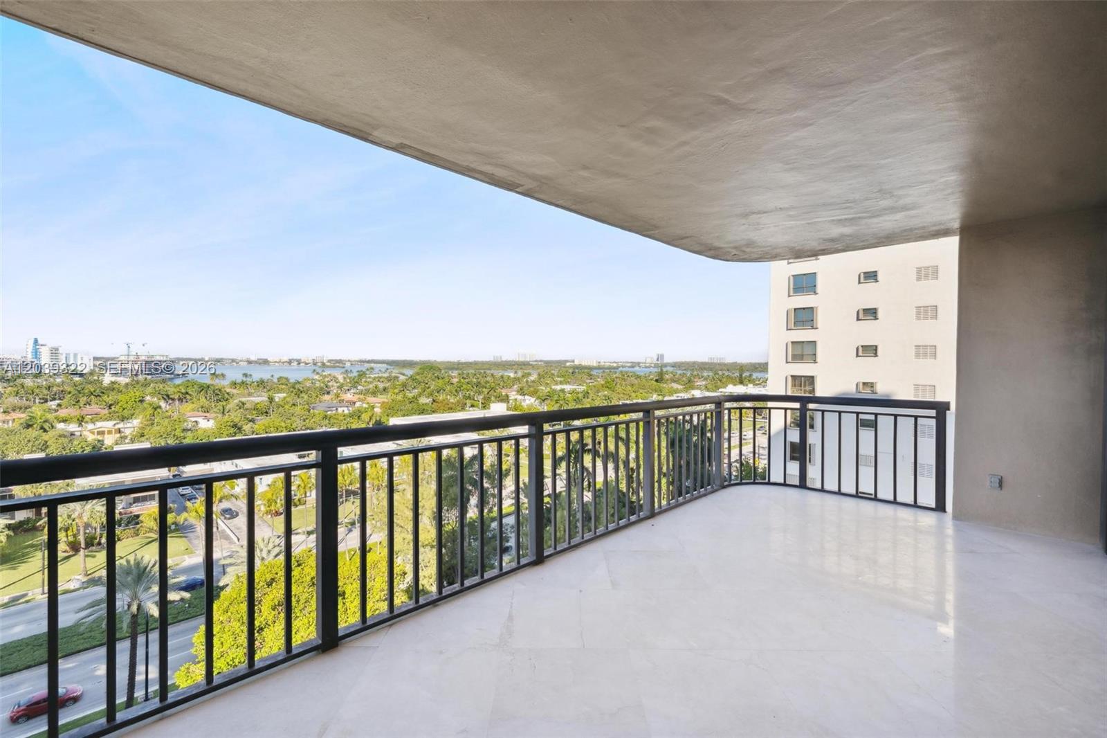 A spacious balcony with a white tiled floor and black metal railings overlooks a landscape — 10175 Collins Ave # 907, Bal Harbour FL 33154, BAL HARBOUR, FL