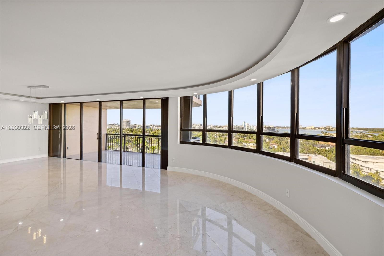 A spacious room with curved floor-to-ceiling windows, marble flooring, and an attached balcony — 10175 Collins Ave # 907, Bal Harbour FL 33154, BAL HARBOUR, FL