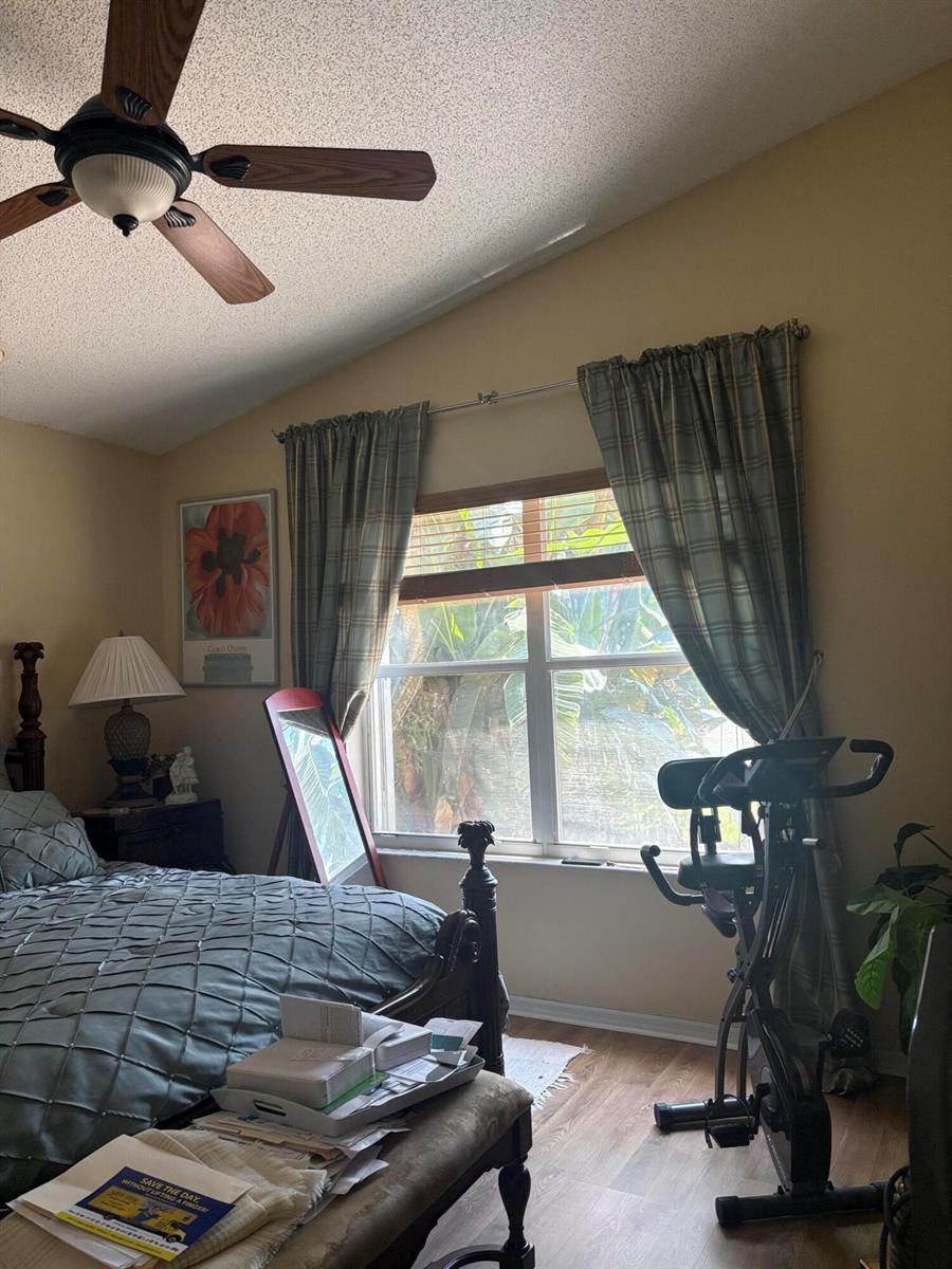 A bedroom features a bed, a ceiling fan, a window with plaid curtains, and exercise equipment — 9815 Lemonwood Drive, Boynton Beach FL 33437, BOYNTON BEACH, FL