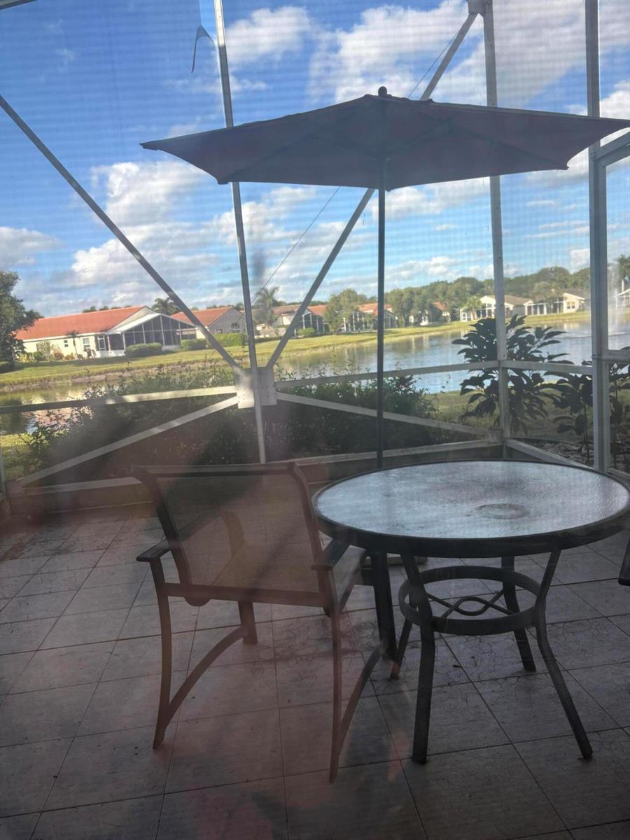 A screened-in patio features a glass-topped table, a chair, and an umbrella overlooking a lake — 9815 Lemonwood Drive, Boynton Beach FL 33437, BOYNTON BEACH, FL
