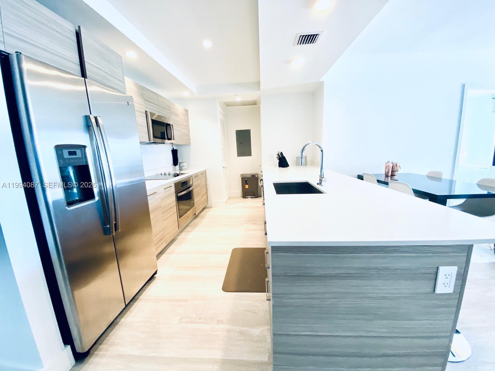 A modern kitchen features light wood cabinetry, stainless steel appliances, and a white quartz island — 121 NE 34th St # 807, Miami FL 33137, MIAMI, FL