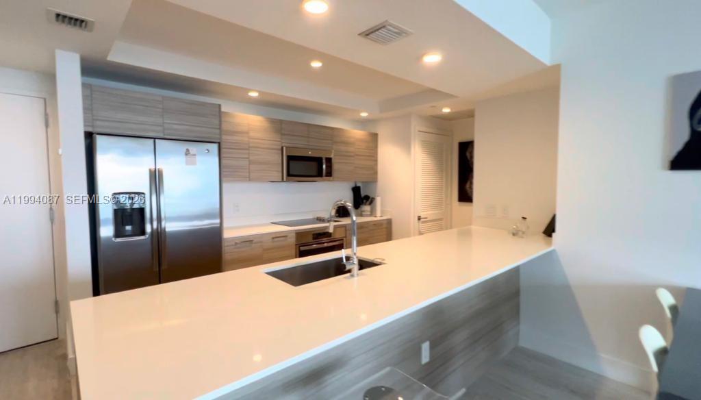 A modern kitchen features light wood cabinetry, white countertops, and stainless steel appliances — 121 NE 34th St # 807, Miami FL 33137, MIAMI, FL