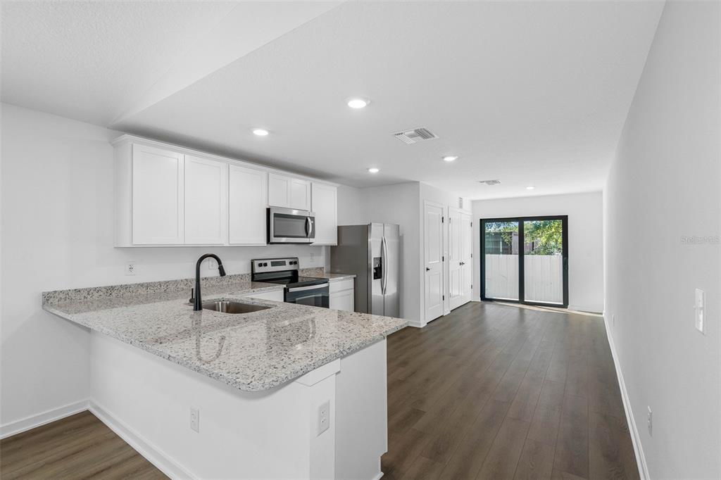 A kitchen with white cabinets, granite countertops, and stainless steel appliances opens to a living area — 14057 CANDIA STREET, SPRING HILL, FL