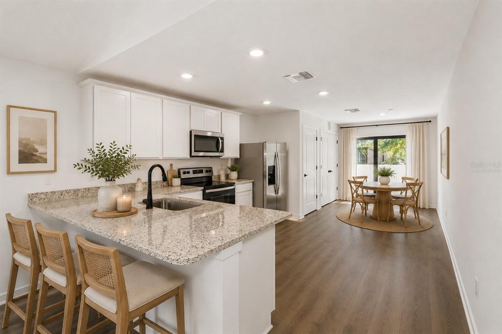 A kitchen with white cabinets, granite countertops, and an island opens to a dining area — 14057 CANDIA STREET, SPRING HILL, FL