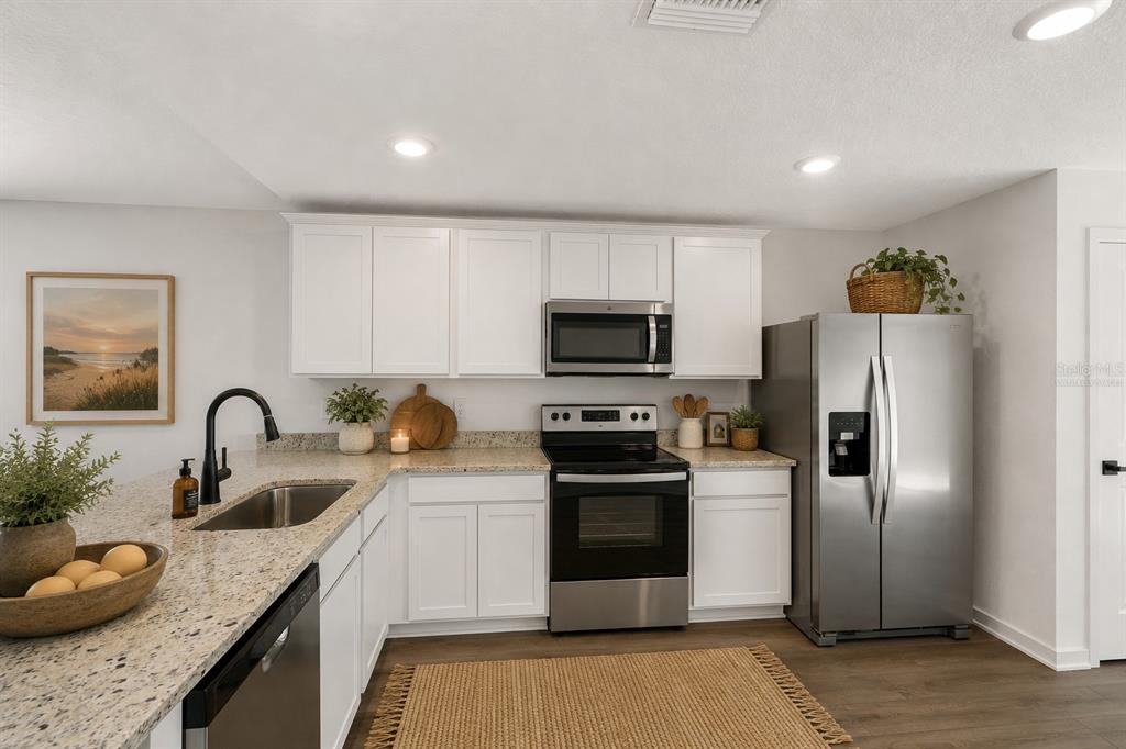 A kitchen features white cabinets, granite countertops, stainless steel appliances, and a woven area rug — 14057 CANDIA STREET, SPRING HILL, FL
