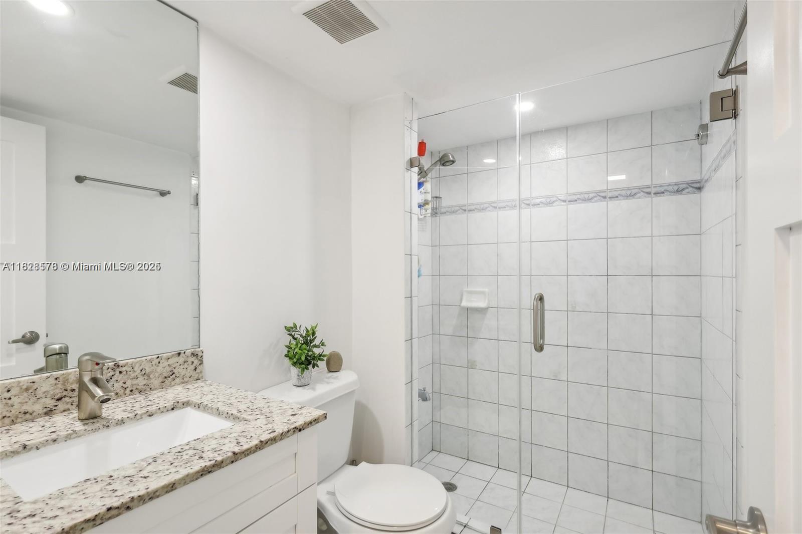 A bathroom features a granite vanity, white cabinets, a toilet, and a tiled glass shower — 2401 Collins Ave # 1011, Miami Beach FL 33140, MIAMI BEACH, FL
