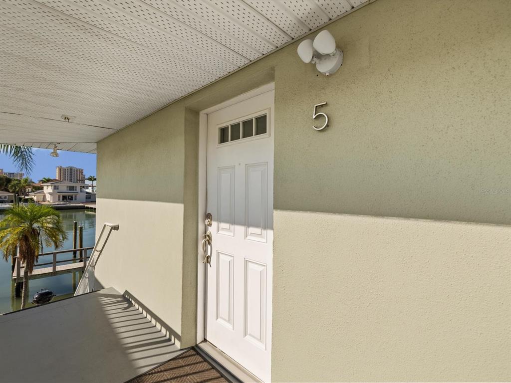 A white front door with the number five is located on a covered exterior walkway — 185 BRIGHTWATER DRIVE UNIT 5, CLEARWATER BEACH, FL
