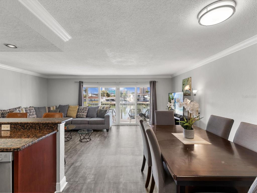 An open-concept living and dining area features wood-look flooring, a granite kitchen island, and balcony — 185 BRIGHTWATER DRIVE UNIT 5, CLEARWATER BEACH, FL