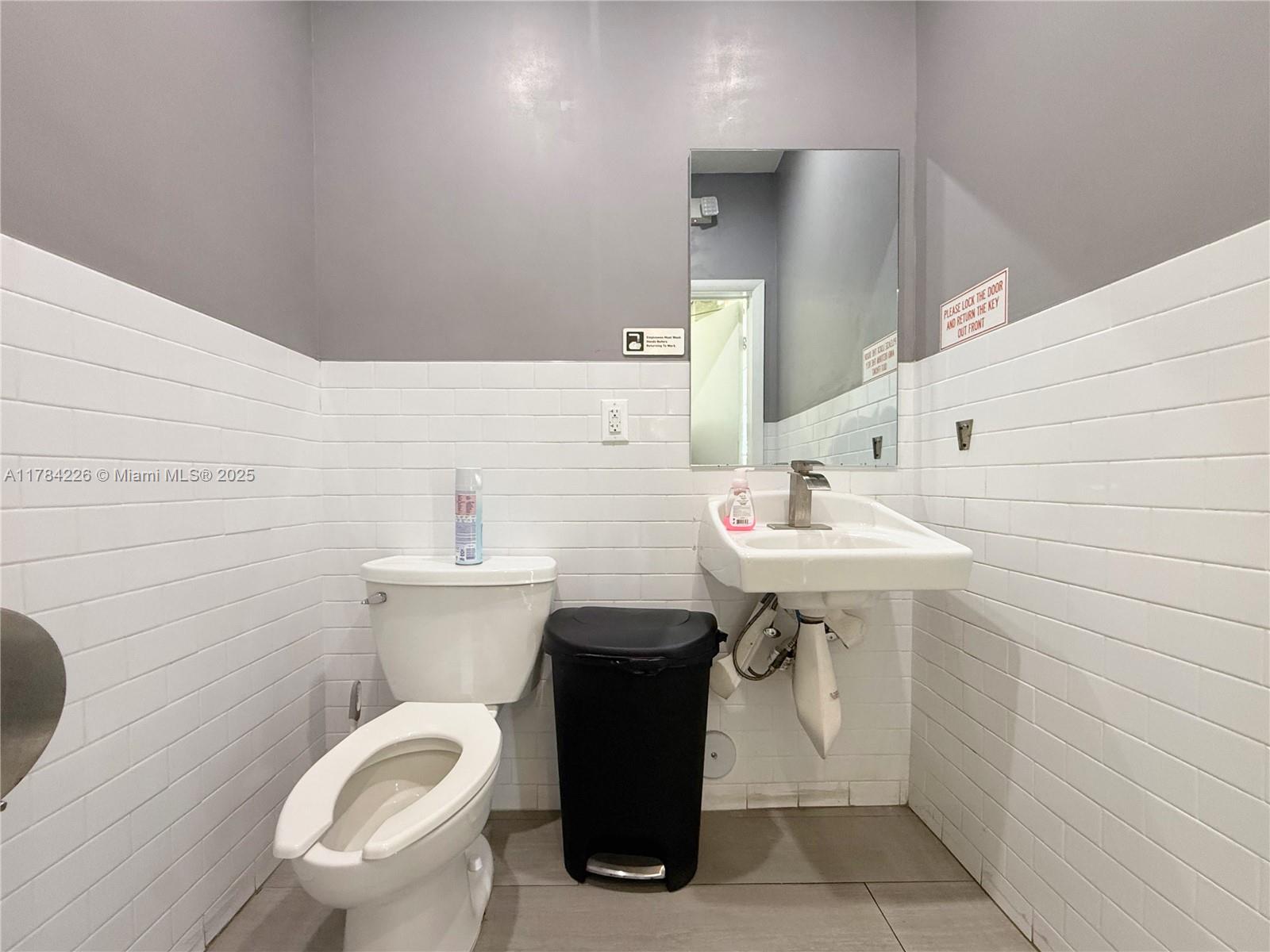 A small bathroom features a white toilet, a wall-mounted sink, and white subway tile walls — E Las Olas Blvd, Fort Lauderdale FL 33316, FORT LAUDERDALE, FL