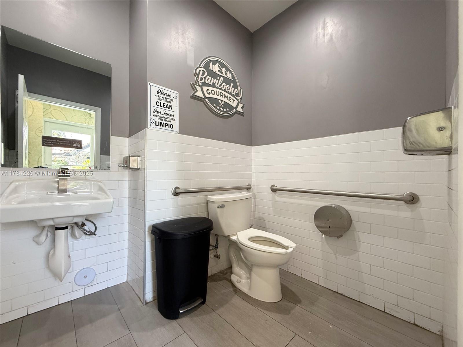 A commercial restroom features white subway tile walls, a toilet with grab bars, and a sink — E Las Olas Blvd, Fort Lauderdale FL 33316, FORT LAUDERDALE, FL