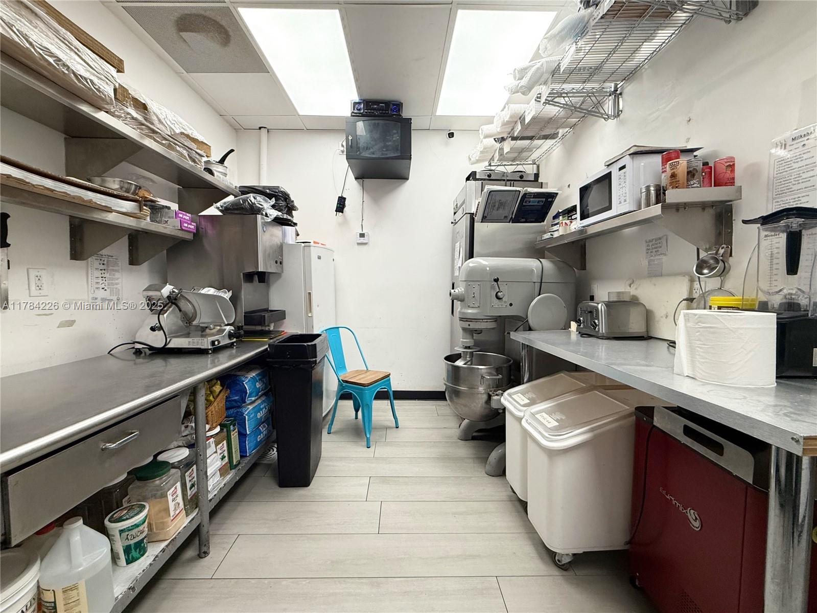A commercial kitchen features stainless steel counters, a large mixer, shelving, and a blue chair — E Las Olas Blvd, Fort Lauderdale FL 33316, FORT LAUDERDALE, FL