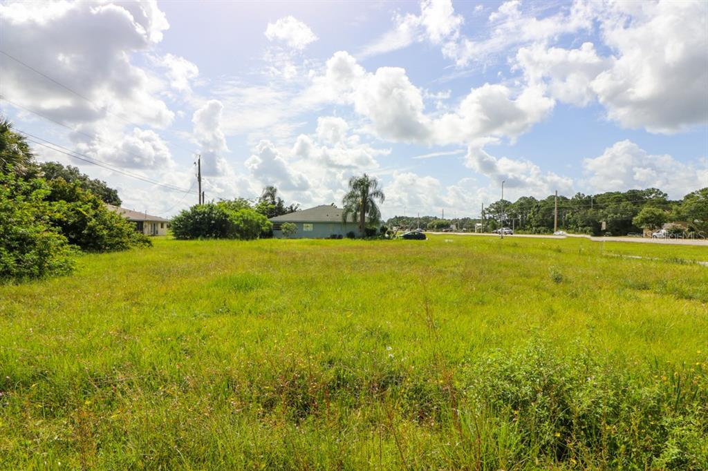 A large, grassy vacant lot sits under a bright, cloudy sky near a residential street — 12000 S TAMIAMI LOT 17 &18 TRAIL UNIT Front, NORTH PORT, FL