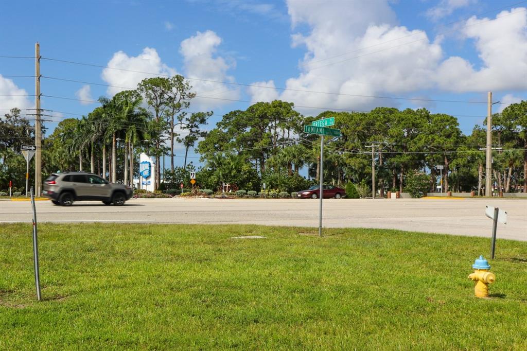 A street intersection with a fire hydrant, a grassy foreground, and a passing car — 12000 S TAMIAMI LOT 17 &18 TRAIL UNIT Front, NORTH PORT, FL