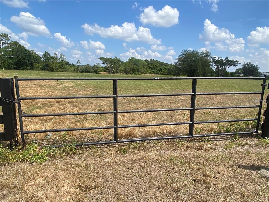 A metal gate stands in front of a large, open grassy field under a blue sky — 9070 STATE ROAD 33, GROVELAND, FL