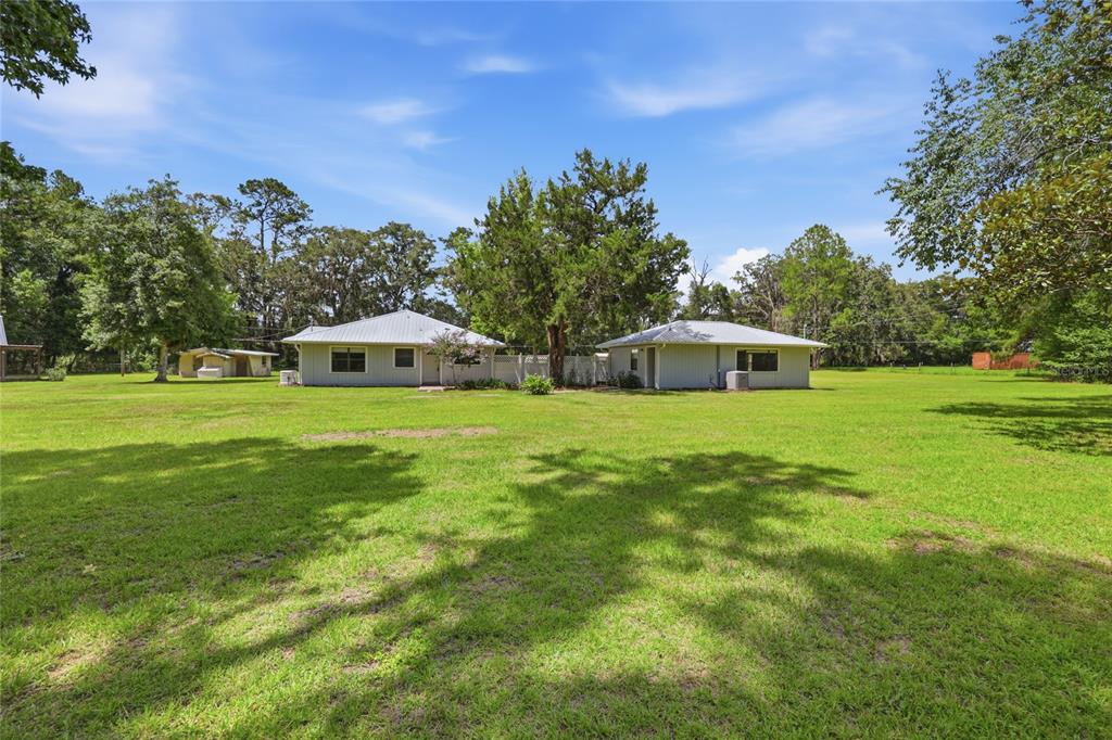 A wide shot of a light-colored house with a metal roof on a grassy lot — 16310 NW 40TH PLACE, NEWBERRY, FL