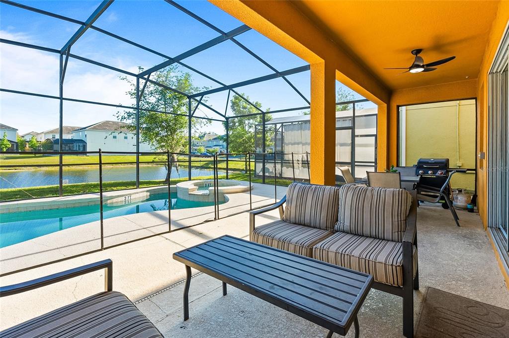 A covered patio with outdoor furniture overlooks a screened-in pool and a lake — 4445 SHIVA LOOP, KISSIMMEE, FL