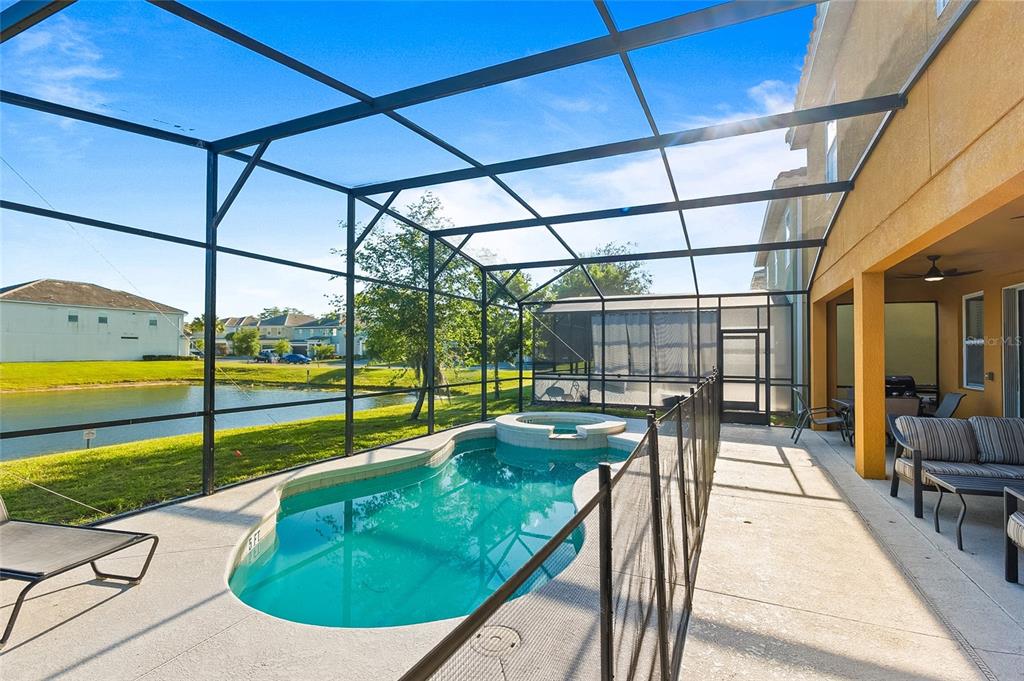A screened-in pool and spa area with a patio overlooking a pond — 4445 SHIVA LOOP, KISSIMMEE, FL