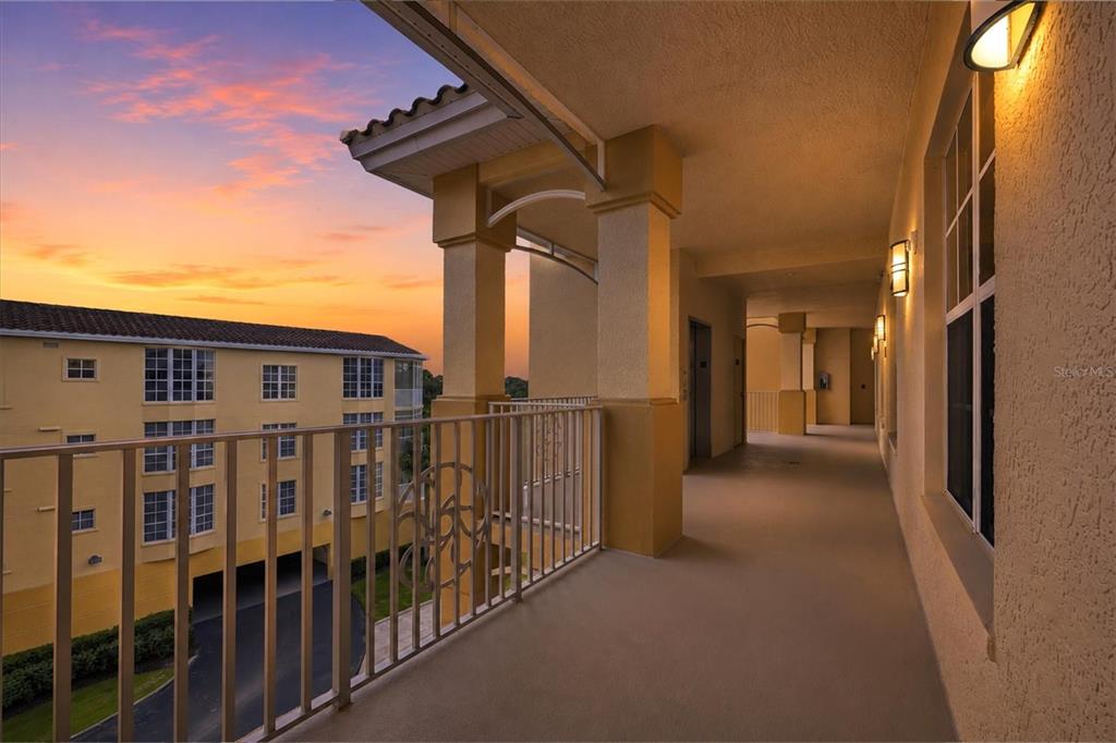 A covered outdoor balcony walkway overlooks a neighboring yellow apartment building at sunset — 6474 WATERCREST WAY UNIT 403, LAKEWOOD RANCH, FL