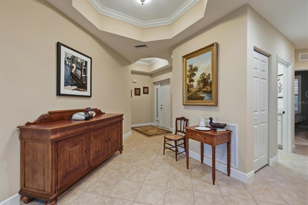 A tiled foyer features a wooden sideboard, a small table with a chair, and artwork — 6474 WATERCREST WAY UNIT 403, LAKEWOOD RANCH, FL