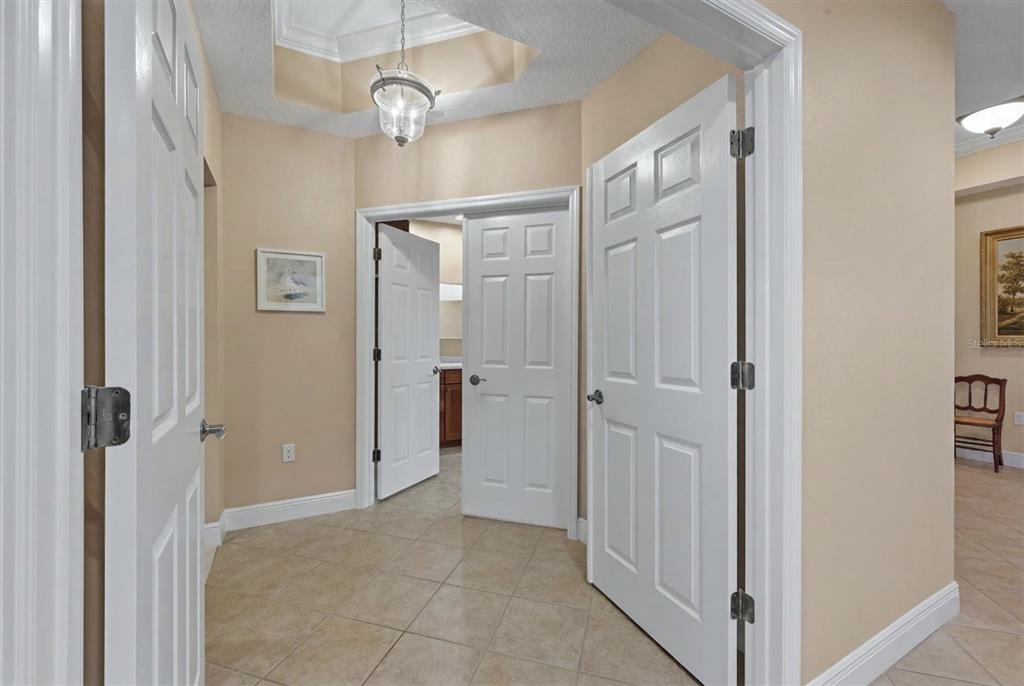 A tiled hallway features white doors, a tray ceiling with a pendant light, and beige walls — 6474 WATERCREST WAY UNIT 403, LAKEWOOD RANCH, FL