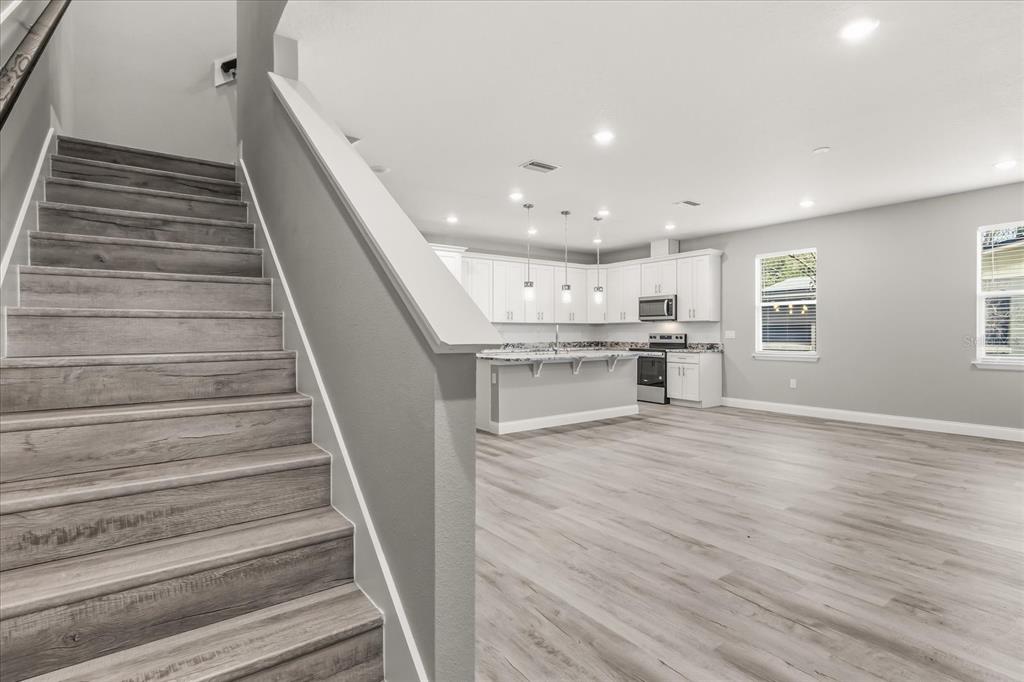 A staircase with wood-look flooring leads down to an open kitchen with white cabinets — 2226 SOUTHWEST ROAD, SANFORD, FL