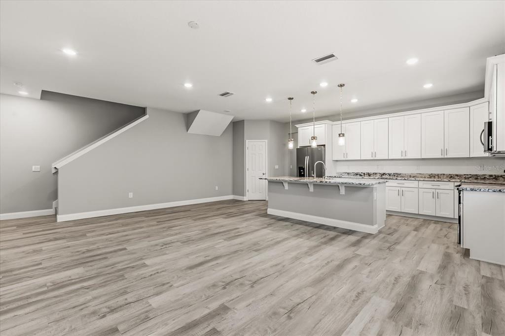 A modern kitchen with white cabinets, a granite island, and wood-look flooring in an open space — 2226 SOUTHWEST ROAD, SANFORD, FL