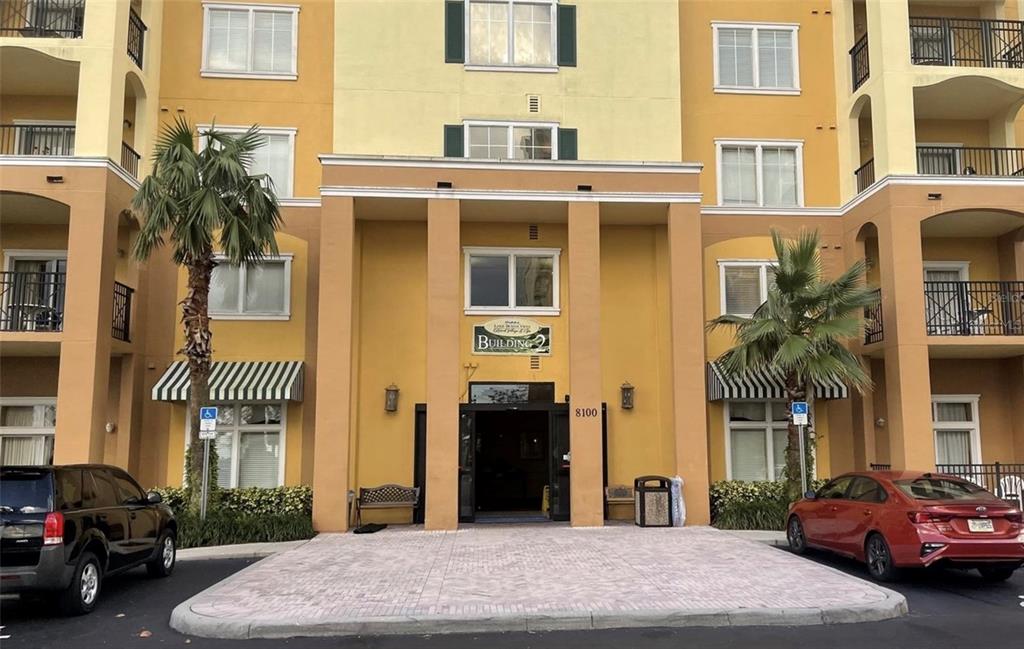 The exterior of a multi-story apartment building features a tan facade, palm trees, and parking — 8100 POINCIANA BOULEVARD UNIT 2203, ORLANDO, FL