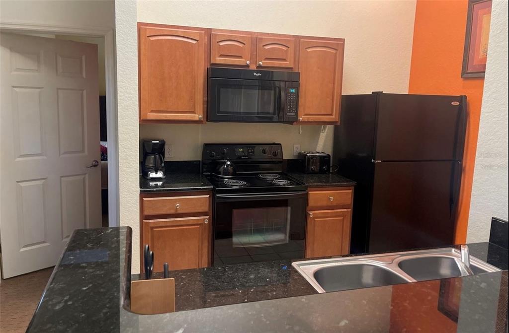A kitchen features wood cabinets, black appliances, and dark granite countertops with a double sink — 8100 POINCIANA BOULEVARD UNIT 2203, ORLANDO, FL