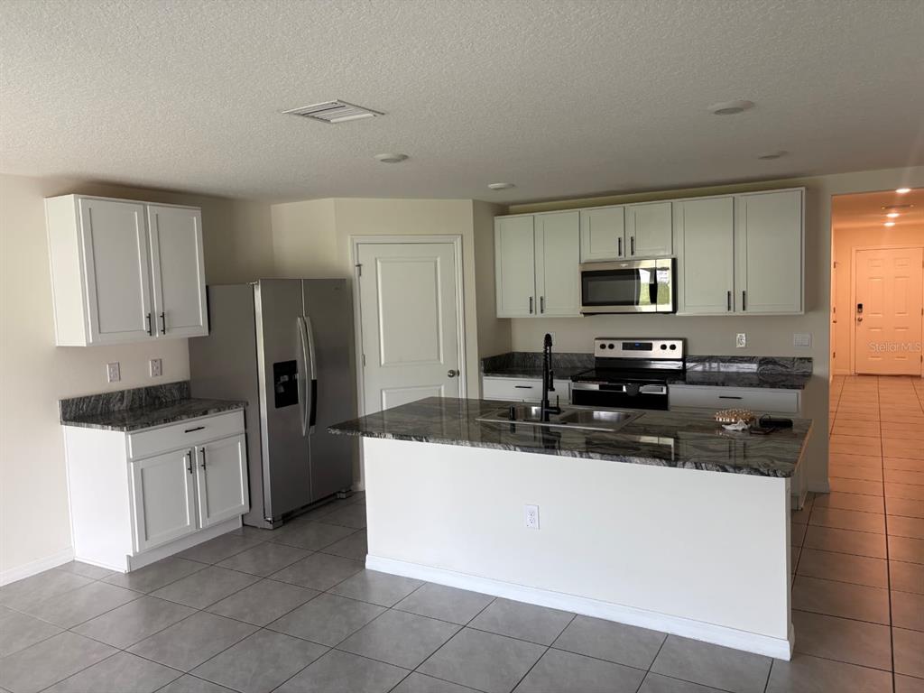 A kitchen features white cabinets, granite countertops, a stainless steel refrigerator, and a center island — 3933 AUTUMN AMBER DRIVE, SPRING HILL, FL