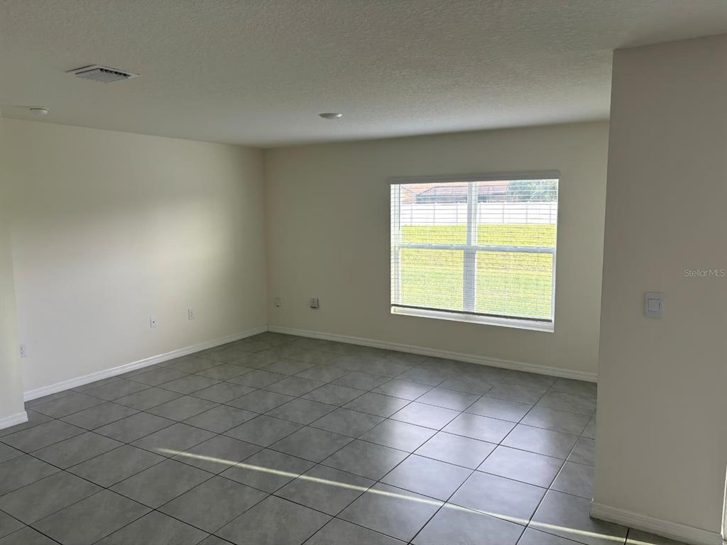 An empty room with gray tile flooring, beige walls, and a window overlooking a yard — 3933 AUTUMN AMBER DRIVE, SPRING HILL, FL