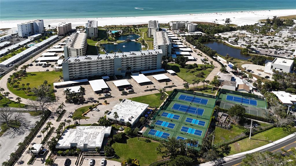 Aerial view of a beachfront condominium complex featuring tennis courts, swimming pools, and parking areas — 5770 MIDNIGHT PASS ROAD UNIT 301, SARASOTA, FL