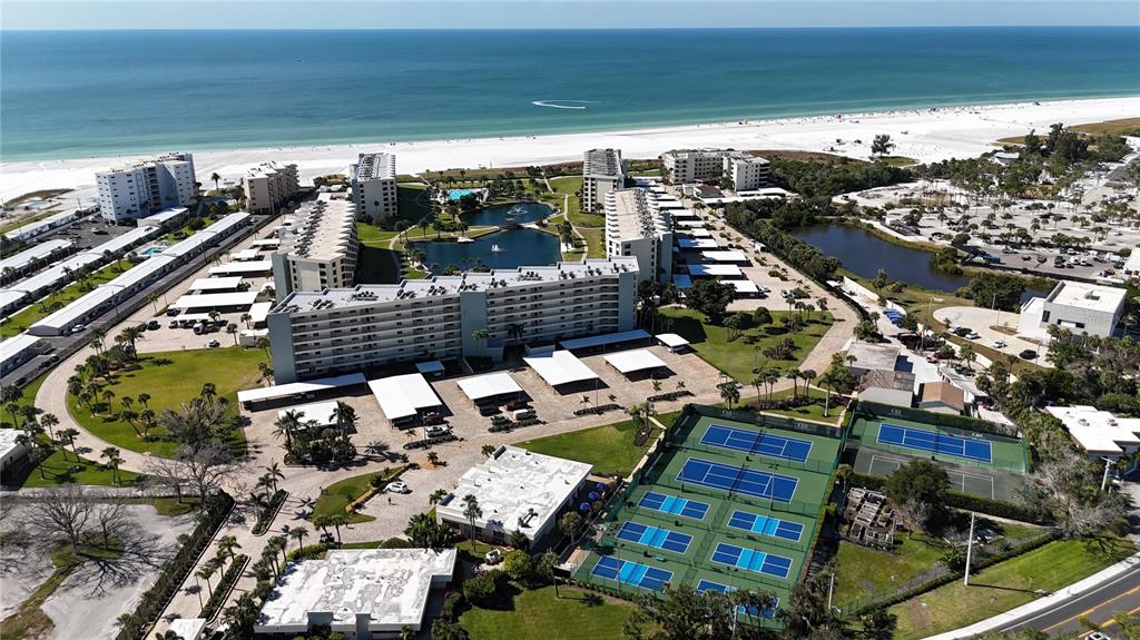 An aerial view shows a coastal resort with multi-story buildings, swimming pools, and tennis courts — 5770 MIDNIGHT PASS ROAD UNIT 301, SARASOTA, FL