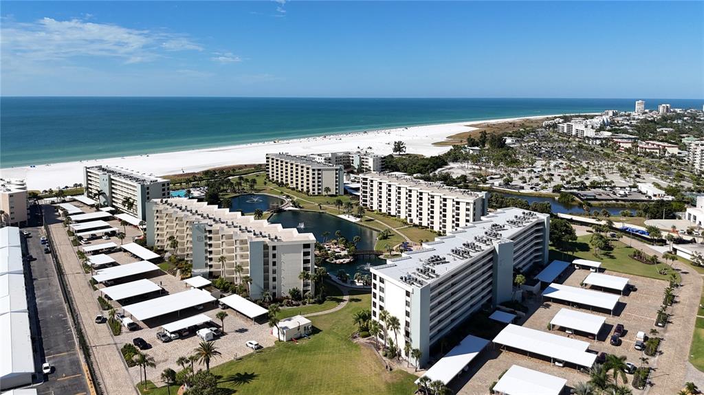 An aerial view shows multi-story apartment buildings with covered parking lots near a sandy beach — 5770 MIDNIGHT PASS ROAD UNIT 301, SARASOTA, FL