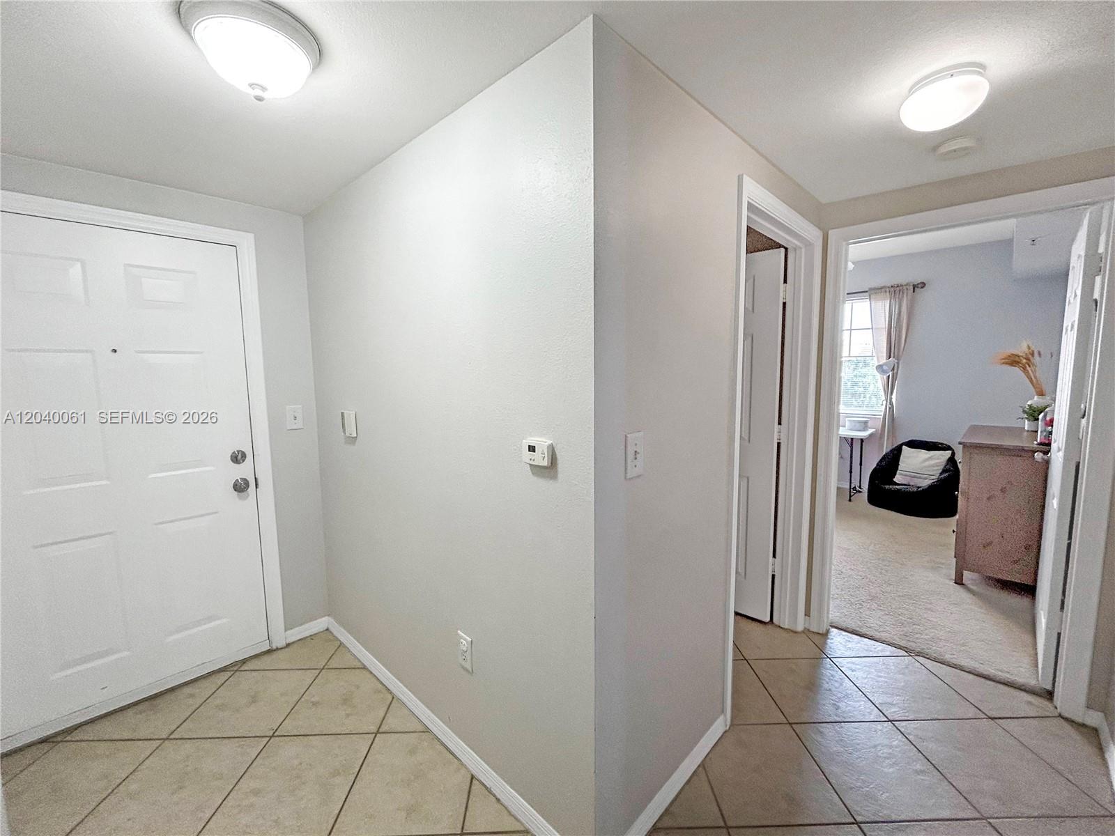 An entryway with tile flooring leads to a hallway and a bedroom with carpet — 6458 Emerald Dunes Dr # 303, West Palm Beach FL 33411, WEST PALM BEACH, FL