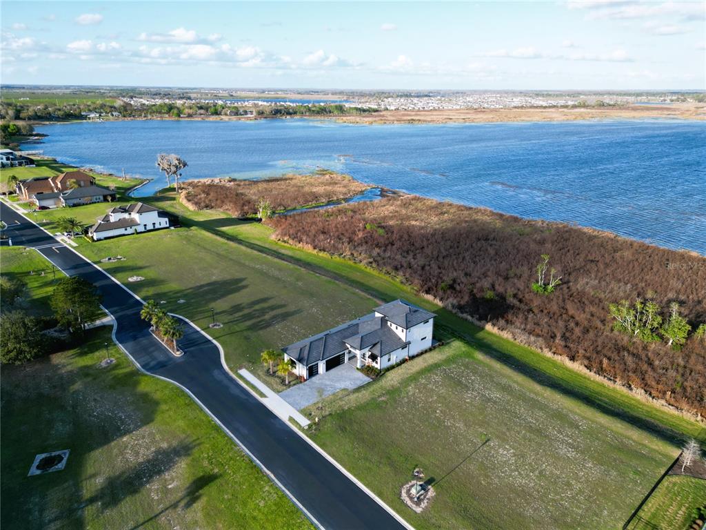 An aerial view shows a modern house situated on a large lot beside a lake — 344 CALADIUM AVENUE, LAKE ALFRED, FL