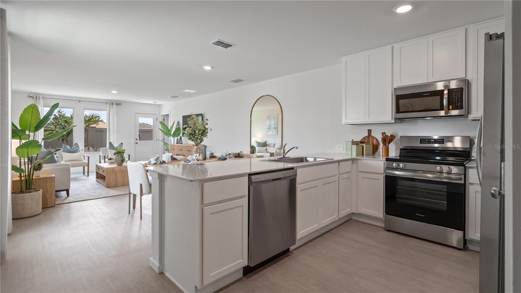 A bright, open-concept kitchen features white cabinetry, stainless steel appliances, and views of the living area — 277 CERAMIC COURT, GROVELAND, FL
