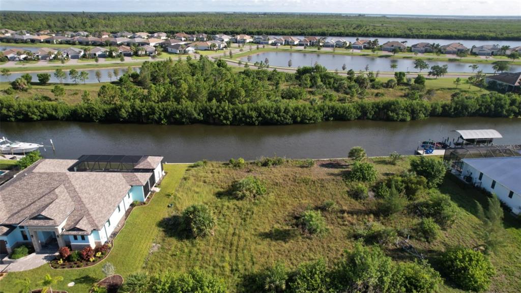 An aerial view shows a vacant waterfront lot situated between two houses along a canal — 15076 LEIPZIG CIRCLE, PORT CHARLOTTE, FL