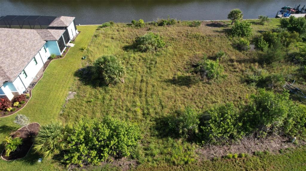 An aerial view shows a vacant, grassy residential lot situated next to a house and canal — 15076 LEIPZIG CIRCLE, PORT CHARLOTTE, FL