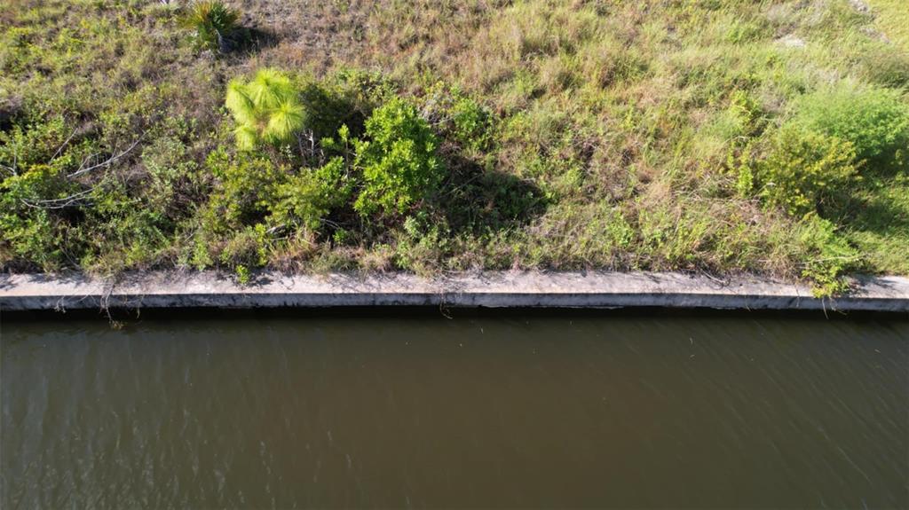 An aerial view shows a concrete seawall bordering a canal next to a grassy bank — 15076 LEIPZIG CIRCLE, PORT CHARLOTTE, FL