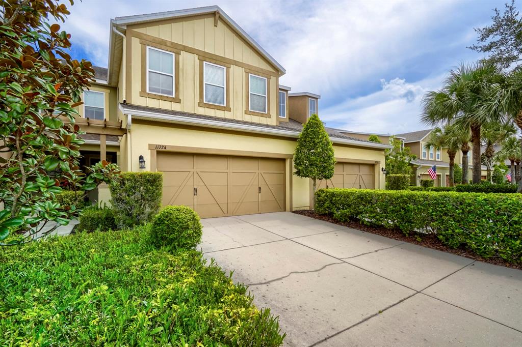 A two-story house exterior features a beige facade, a double garage, and a concrete driveway — 11724 CASA LAGO LANE, TAMPA, FL