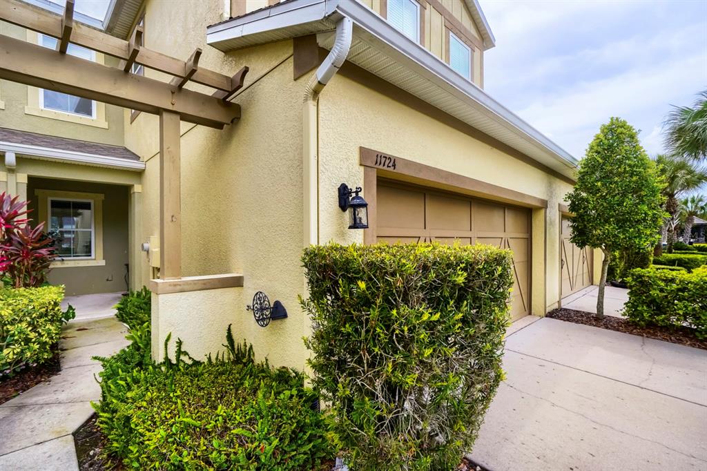 The exterior of a tan house features a garage, a pergola, and manicured landscaping — 11724 CASA LAGO LANE, TAMPA, FL