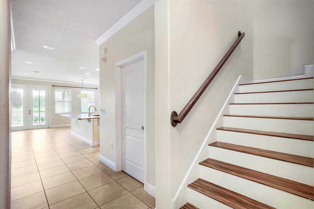 A staircase with wood treads and a white railing sits beside a tiled hallway entrance — 11724 CASA LAGO LANE, TAMPA, FL
