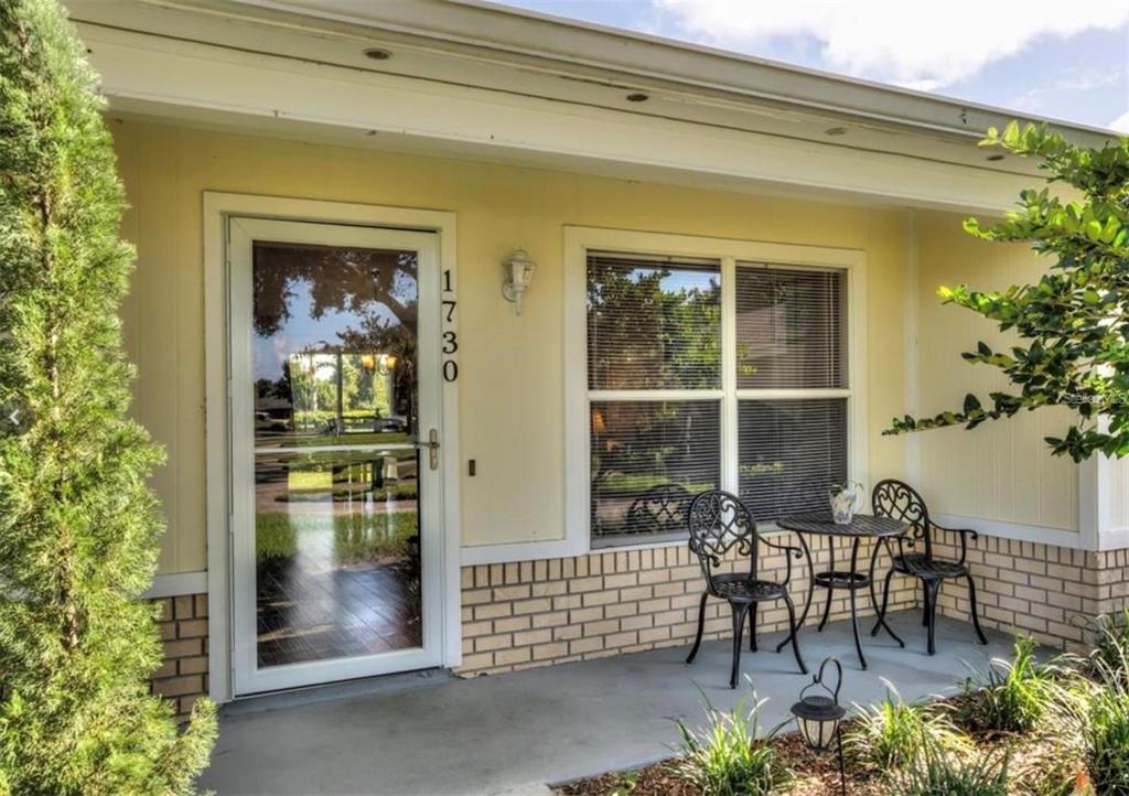 A yellow house exterior features a front door with a storm door and a patio — 1730 TROPICAL COURT, TAVARES, FL